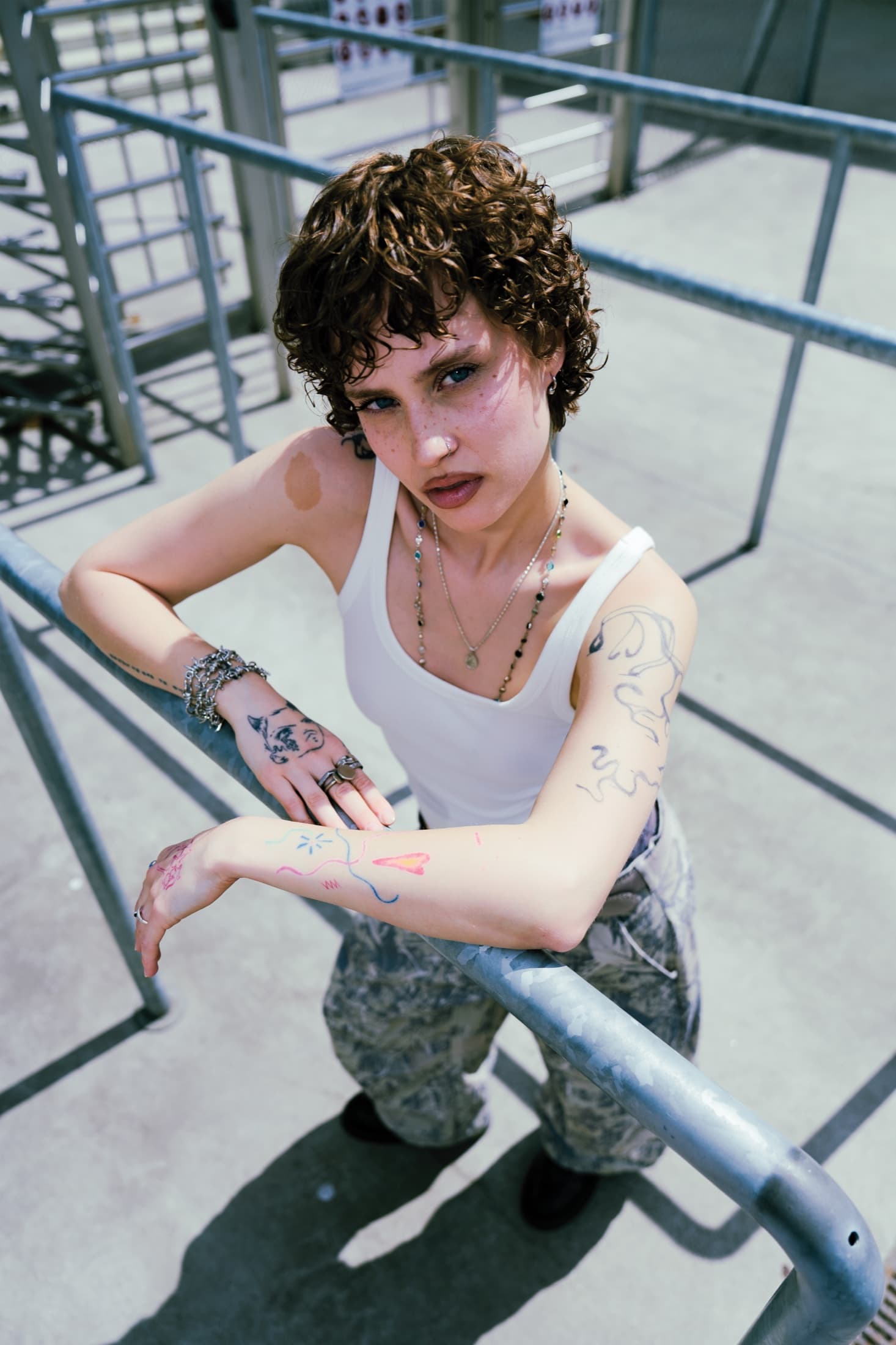 Looking up from the turnstile rails – red fineline on her hand, curls backlit by the sun.