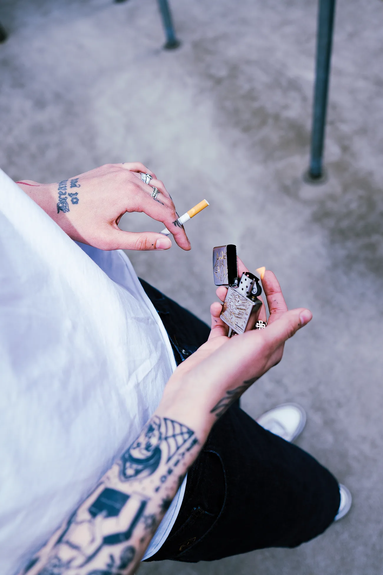 Tattooed hands with silver rings over an engraved Zippo, seen from above.