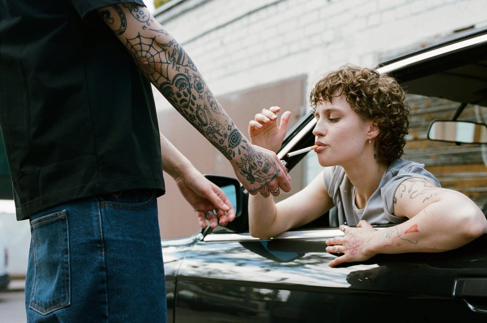 A cigarette being lit through the car window – two hands, a flame, curly hair in summer air.
