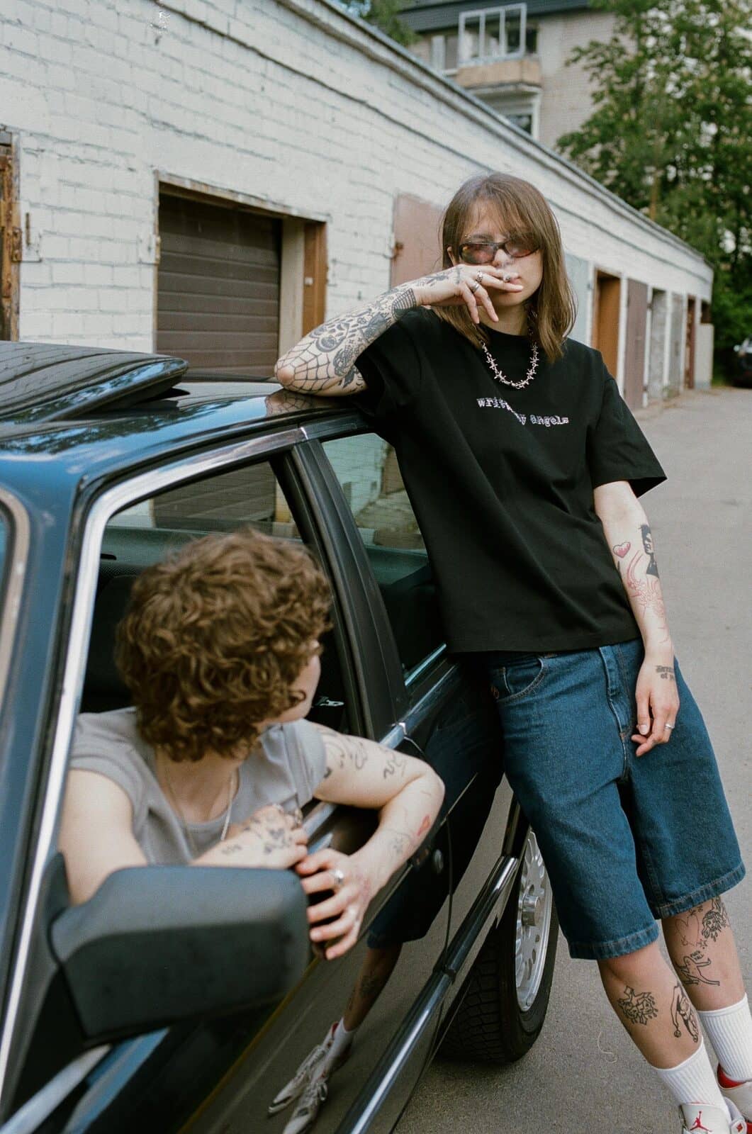 Two figures and the black car by the garages – hair and t-shirt moving in a light breeze.
